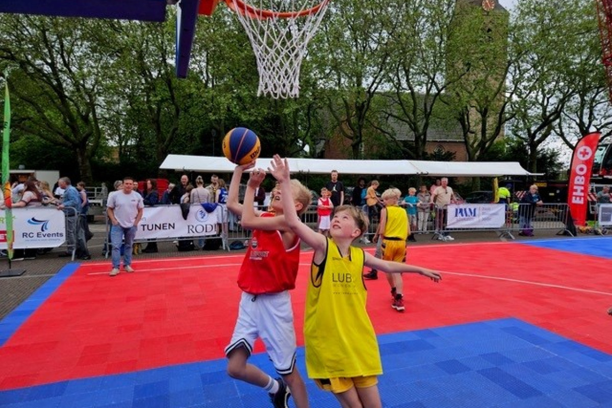 kinderen spelen buiten basketbal op een rood-blauw veld.